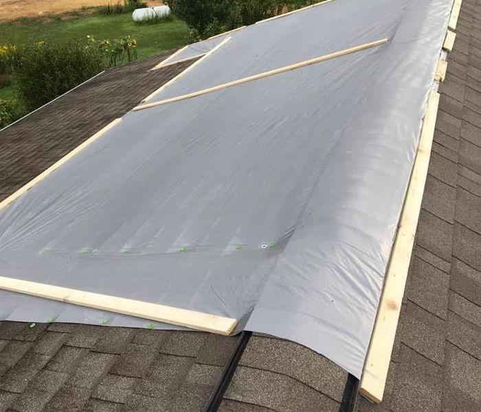 Roof covered with grey tarp after storm tears off shingles